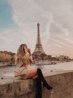 a woman sitting on the edge of a wall looking at the eiffel tower