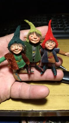 three small knitted elves sitting on top of a persons hand