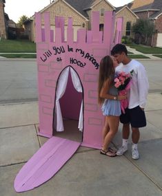 a man and woman standing in front of a pink castle with writing on the door