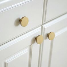 two brass knobs are on the white cabinet doors