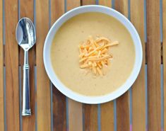 a bowl of soup with cheese on top and a spoon next to it sitting on a wooden table