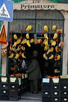 a man standing in front of a fruit stand with bananas hanging from it's ceiling