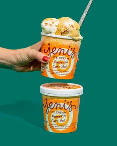 two ice cream cups with orange and white toppings, one being held up by a woman's hand