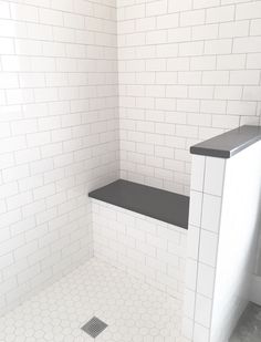 an empty white tiled bathroom with black counter tops and floor tiles on the shower wall