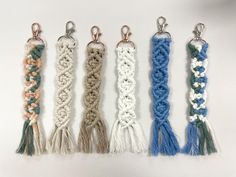 five different colored crocheted tassels are lined up on a white surface