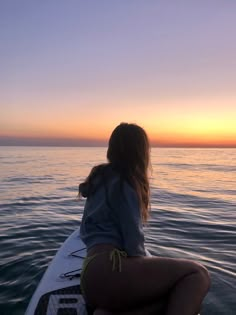 a woman sitting on top of a surfboard in the middle of the ocean at sunset