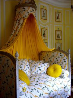 a canopy bed with yellow pillows on it in the corner of a room filled with pictures