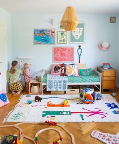 two children playing in a room with toys on the floor and artwork on the wall