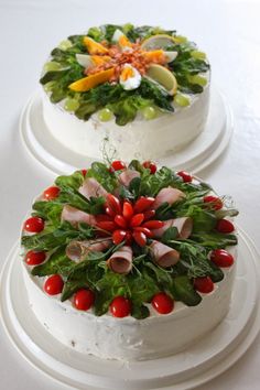 two cakes decorated with flowers and fruits on top of each other, sitting on white plates