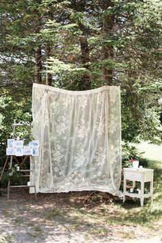 a white bed sitting in the middle of a forest next to a table and chair