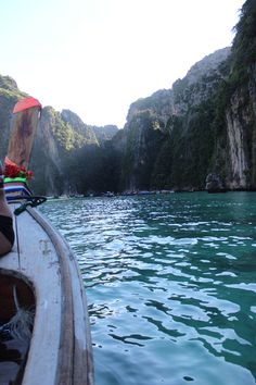 a person on a boat in the water near some mountains and cliffs, with a red umbrella over their head