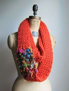 an orange knitted scarf with multicolored flowers on it sitting on a mannequin