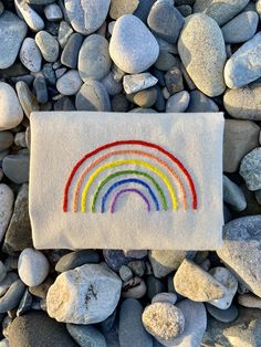 a white towel with a rainbow embroidered on it sitting next to some rocks and stones