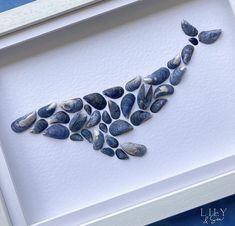 a white framed artwork with blue rocks in the shape of a bird on it's back