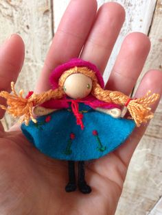 a hand is holding a small doll in it's left hand, wearing a blue dress and pink hat