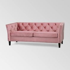 a pink velvet couch with buttons on the back and arms, in front of a white background