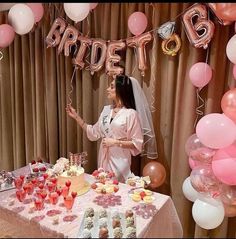 a woman standing in front of a table filled with cakes and desserts next to balloons