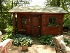 a small wooden shed sitting in the middle of a yard with chairs and tables around it