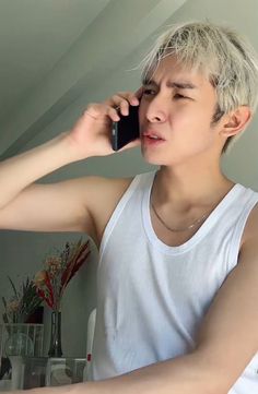 a man talking on a cell phone while wearing a white tank top and silver necklace