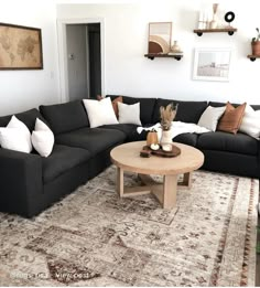 a living room filled with black couches and white pillows on top of a rug