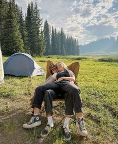 two people are sitting on a lawn chair in the grass near tents and camping equipment