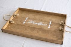 a wooden tray with rope handles and writing on the side that says breakfast in white lettering