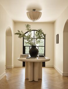 a vase sitting on top of a table next to a plant in a room with wooden floors