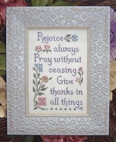 a cross - stitch frame with flowers and words on it, sitting in front of purple flowers