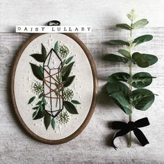 a cross stitch pattern on a wall hanging next to a potted plant with the words daisy lullaby