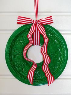 a green wreath with red and white ribbons hanging on the front door ornament