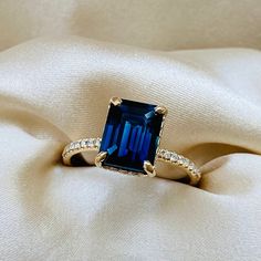 a ring with an emerald colored stone surrounded by small diamonds on top of a white cloth