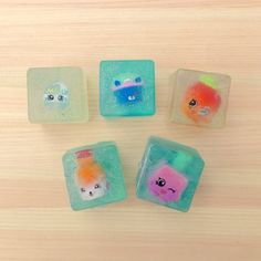 four different colored cubes with faces on them sitting next to each other in front of a wooden surface