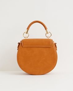 Crafted from certified vegan leather in classic tan, this curved satchel design evokes a sense of country life, reminiscent of a classic equestrian saddle bag. Complete with a top handle, an adjustable cross-body strap and a magnetic fastening, all designed to keep your most precious treasures safe and secure.
  Key features:
  Approx. 21.5 (L) x 19 (H) x 9.5(D) cm
 Outer: 100% Polyurethane; Lining: 100% Polyester
 Wipe clean with damp cloth Equestrian Saddle, Swan Jewelry, Saddle Handbags, Equestrian Chic, Luxury Christmas Gifts, Green Tote, Stylish Handbags, Embroidered Bag, Small Tote