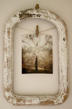 an old white frame hanging on a wall with a tree in the middle and some clothes pins attached to it