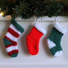 three knitted stockings hanging from a christmas tree ornament on a white mantle