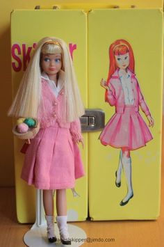 a barbie doll standing in front of a yellow refrigerator with a pink dress on it