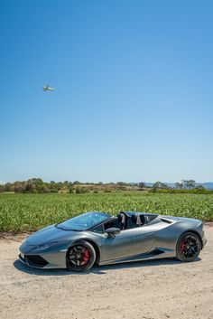 a silver sports car parked on the side of a road near a corn field and an airplane in the sky