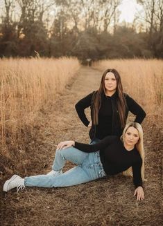 two women sitting on the ground posing for a photo in a field with tall grass