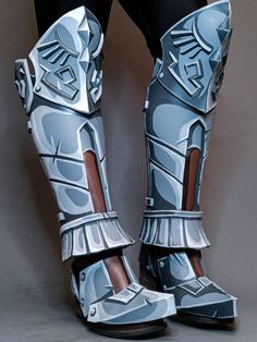 the legs and feet of a person in armor gear, standing against a gray background