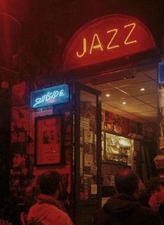 people are sitting at tables in front of a jazz bar with neon signs on the door