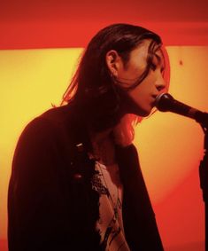 a woman singing into a microphone in front of an orange and red background with the sun behind her