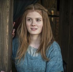 a woman with long red hair standing behind a wooden fence looking at the camera and smiling