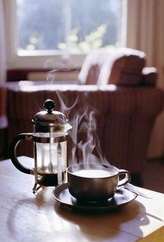 a steaming tea pot on a table next to a coffee cup