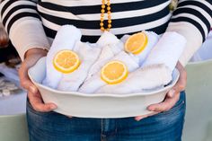 a woman holding a white bowl filled with towels and orange slices on top of it