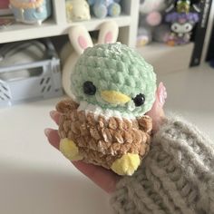 a hand holding a small stuffed animal in it's right hand and wearing a knitted hat