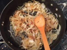 onions being cooked in a pan with a wooden spoon