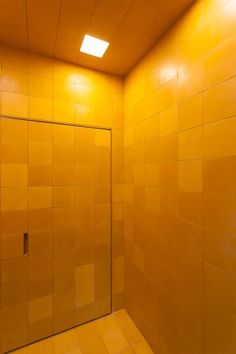 a yellow tiled bathroom with a glass shower door and light on the ceiling above it