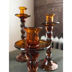 two glass candlesticks sitting on top of a table next to another candle holder