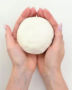 two hands holding a white ball of dough in front of the camera on a white background