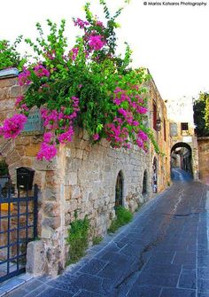 an old stone building with pink flowers growing on it